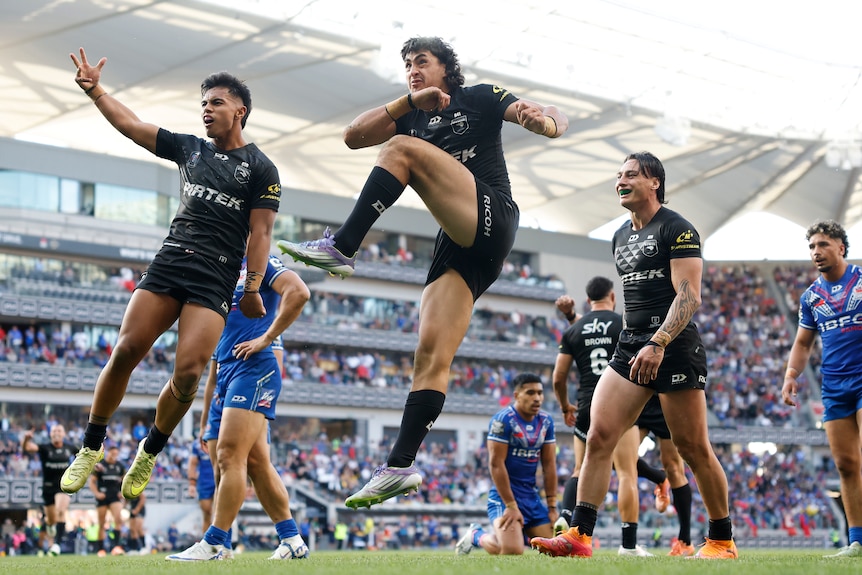 Three rugby league players in black jump up in celebration while players in blue sink to their knees in disappointment