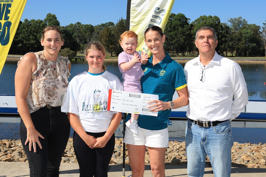 Four people stand and pose for a photo. At the centre is Olympic kayaker Alyce Wood who holds her daughter