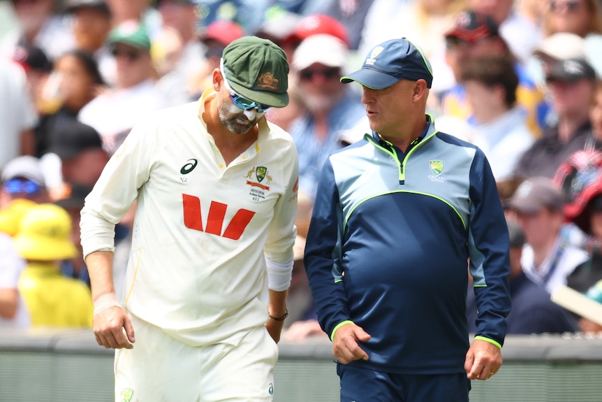 Australia bowler Nathan Lyon leaves the field alongside a Cricket Australia staff member.