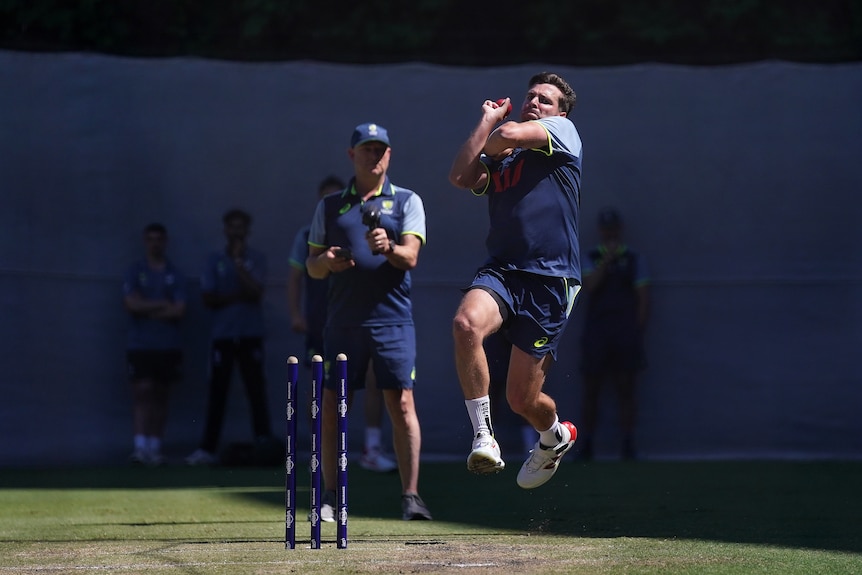 Jhye RIchardson bowls in an Australian cricket training session while a coach watches on.