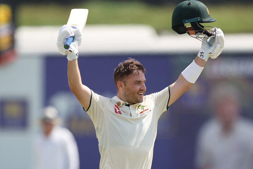 A young, dark-haired cricketer raises his bat and helmet in celebration.