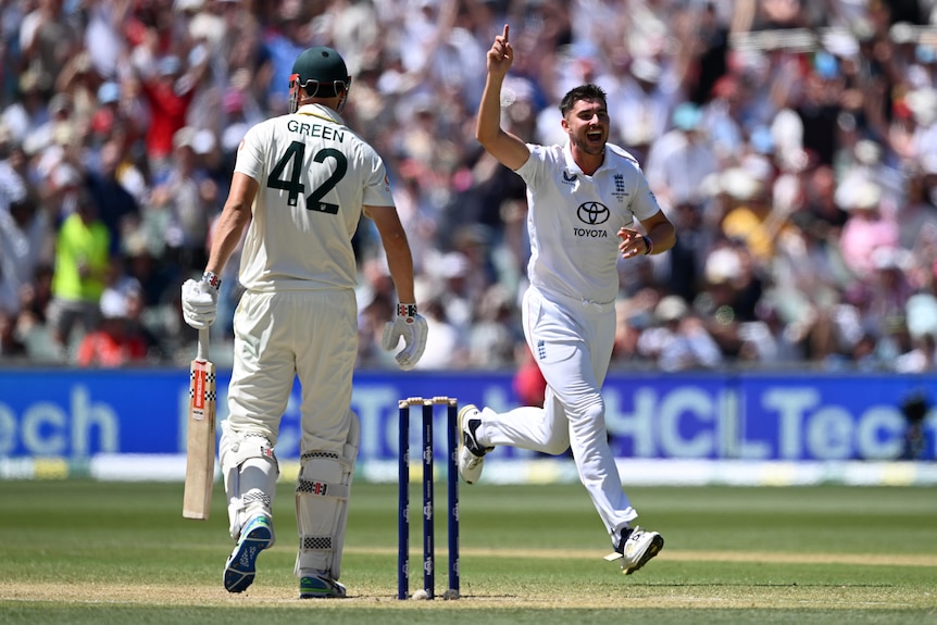 Australia batter Cameron Green, seen from behind, stands on the pitch as England bowler Josh Tongue holds a finger in the air.