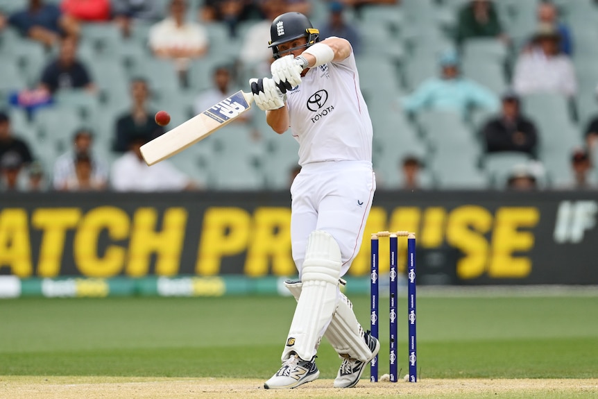 A cricket batter plays a shot to a red ball in front of his stumps