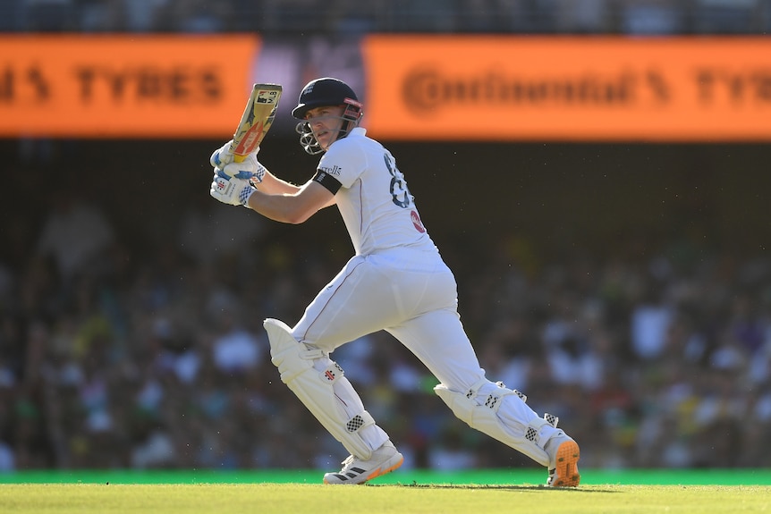 A cricket batter in white plays a shot in afternoon sunshine