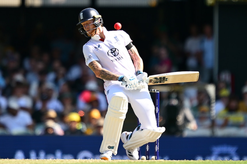 A cricket batter in white and with a blue helmet sways underneath a short pink ball