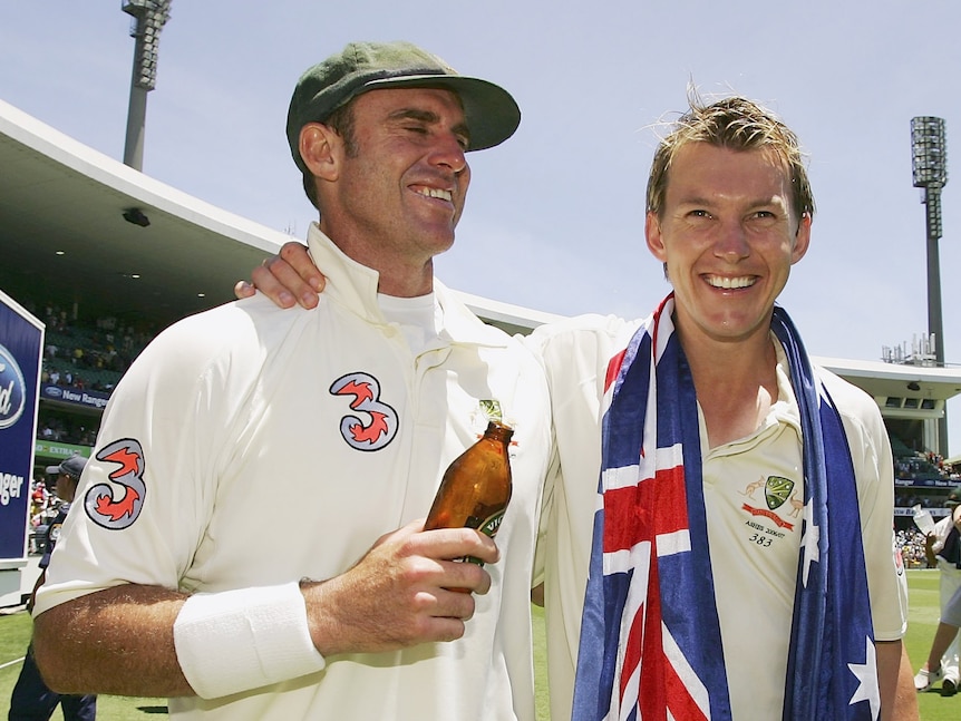 Two Australian cricketers celebrate after an Ashes win, one with a beer and the other with an Australian flag around him.
