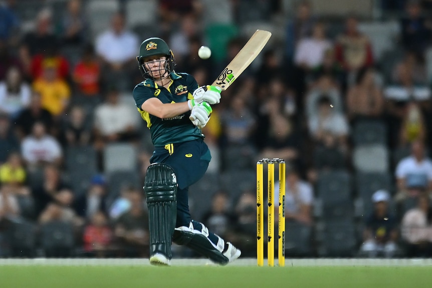An Australian women's cricketer hits the ball down the ground during a T20 international.