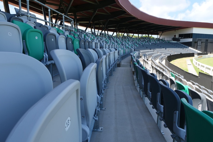 Grandstand seats curving around a pitch with a broadcast box in the background. 
