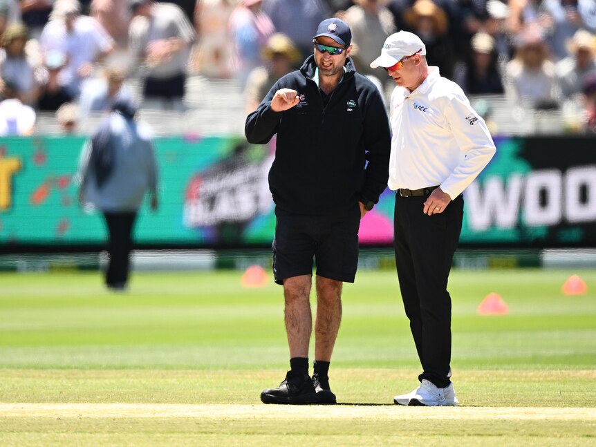 A curator talks to an official as they look at the pitch during a break in a cricket Test at the MCG.