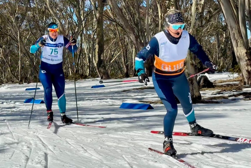 Taryn is skiing behind her guide, who gives her instructions through a speaker attached to their back.