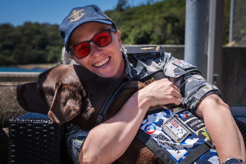 Taryn is smiling as she hugs her assistance dog, Gigi, a chocolate labrador.