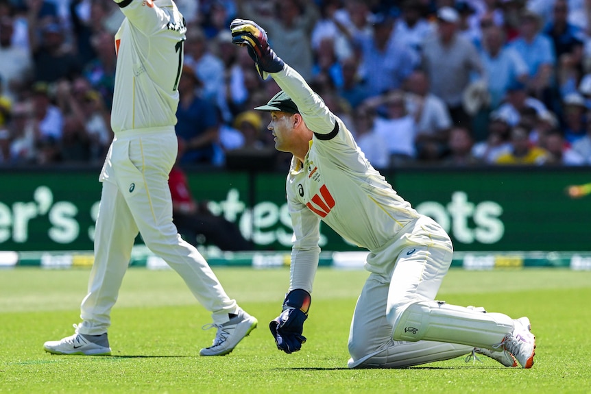 Australia wicketkeeper Alex Carey holds the ball up with one hand while on his knees during a Test.