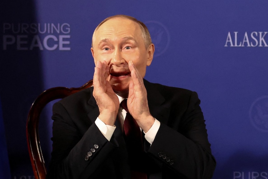 A man in a suit cupping his hands near his mouth and speaking