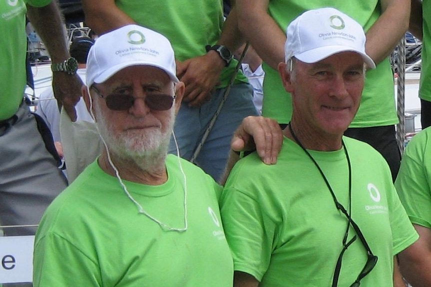 A close-up of two sailors wearing green T-shirts, with crewmates in the same gear behind them. 