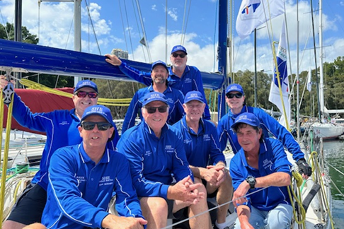 A crew of eight sailors seated or crouching on board a boat, posing before the Sydney to Hobart yacht race.