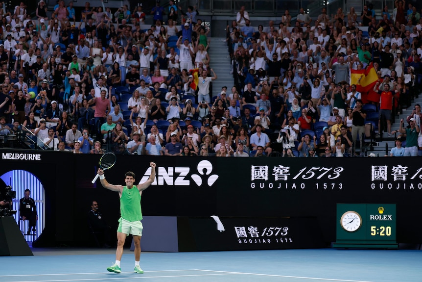 Carlos Alcaraz raises both arms to celebrate as the Australian Open crowd rises.