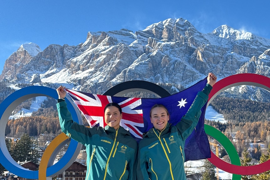 Sarah Blizzard and Desi Johnson stand in front of the Olympic rings with an Australia flag
