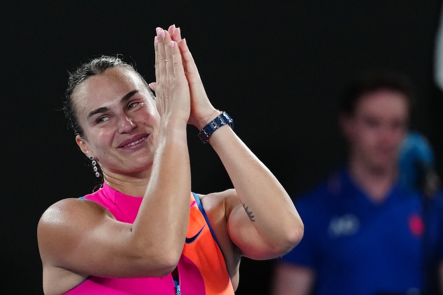 Aryna Sabalenka holds up her hands pressed together thanking the crowd.