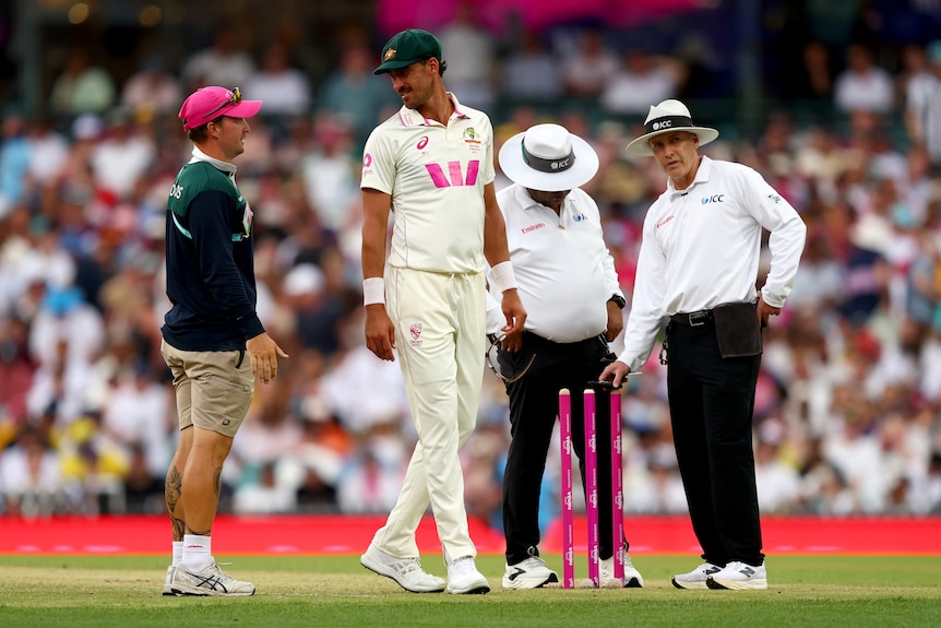Mitchell Starc speaks to a groundskeeper and umpires in the middle of the SCG.