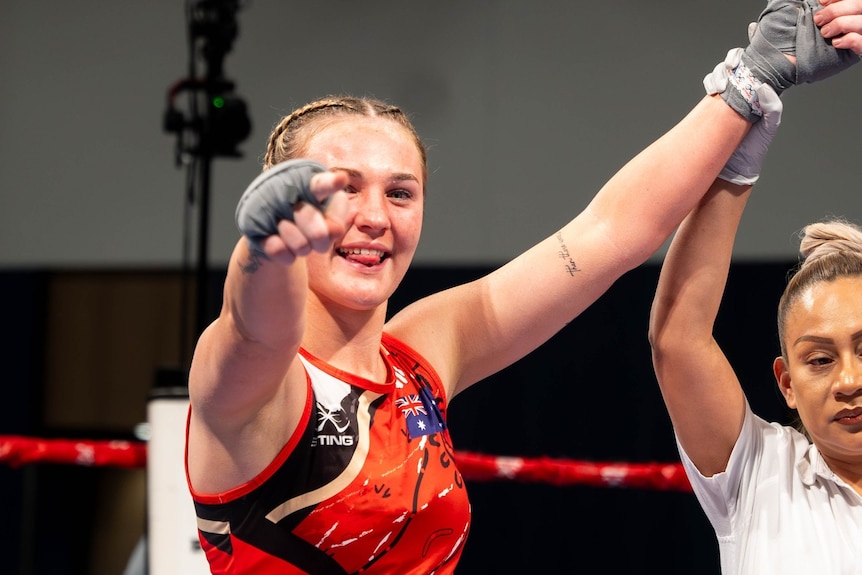 A young woman with pigtails in boxing gear, pointing at the camera with her hand up.