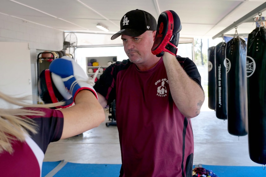 A man in a cap with boxing targets on his hands. 