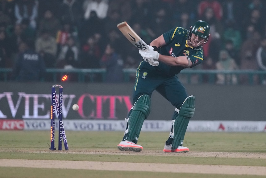 Batter attemps ramp shot and misses white cricket ball, which hits leg stump and dislodges bail