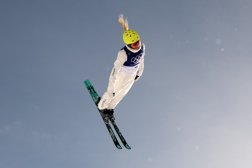 A female skiier in an Olympic bib soars through the air.