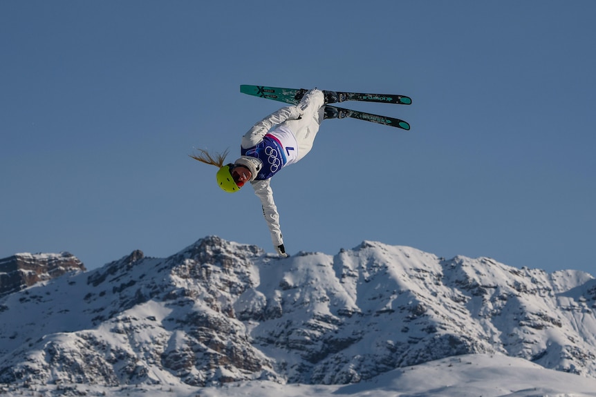 A female Olympic skiier performs an aerial manouevre in an alpine setting.