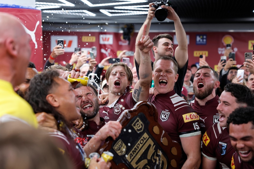 Queensland Maroons players celebrate in the locker room.