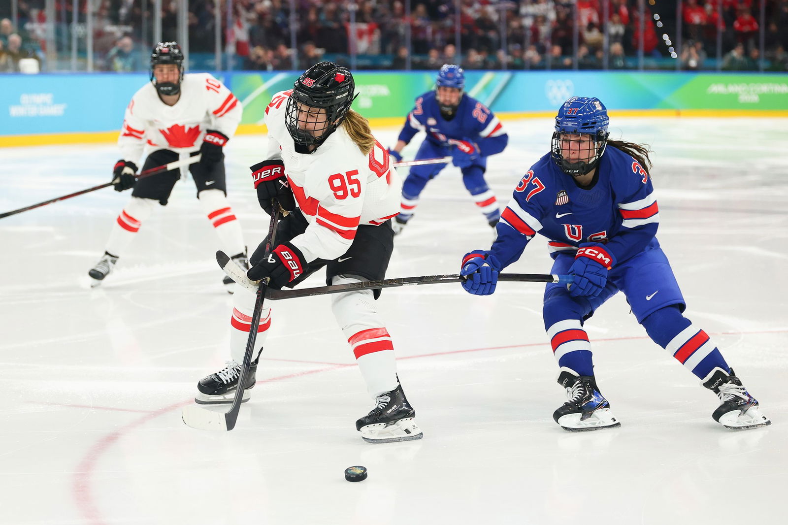 Four hockey players, two in white and tow in blue tussle for the puck