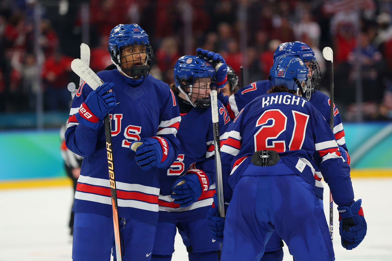 A group of ice hockey players in red and blue celebrate a goal