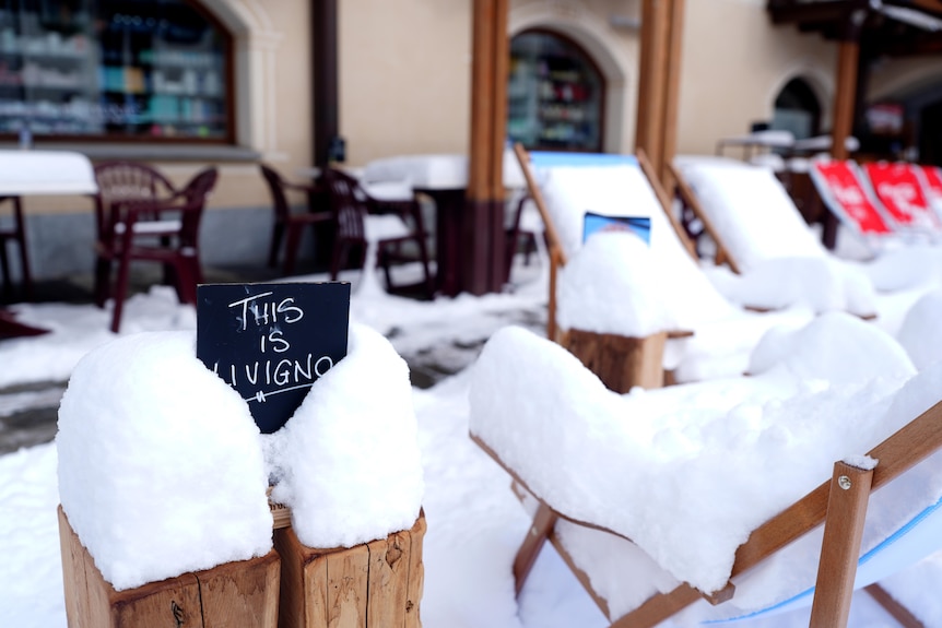 Snow covers chairs and a sign