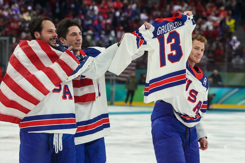 Three ice hockey players skate on the ice, holding the jersey of a teammate who has died