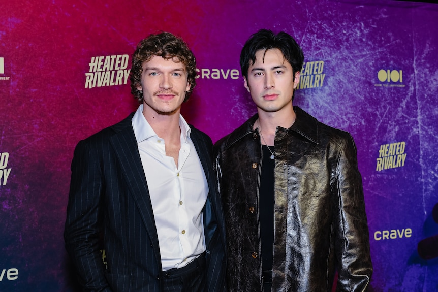 Actors Connor Storrie and Hudson Williams pose for a photo on a red carpet with serious expressions