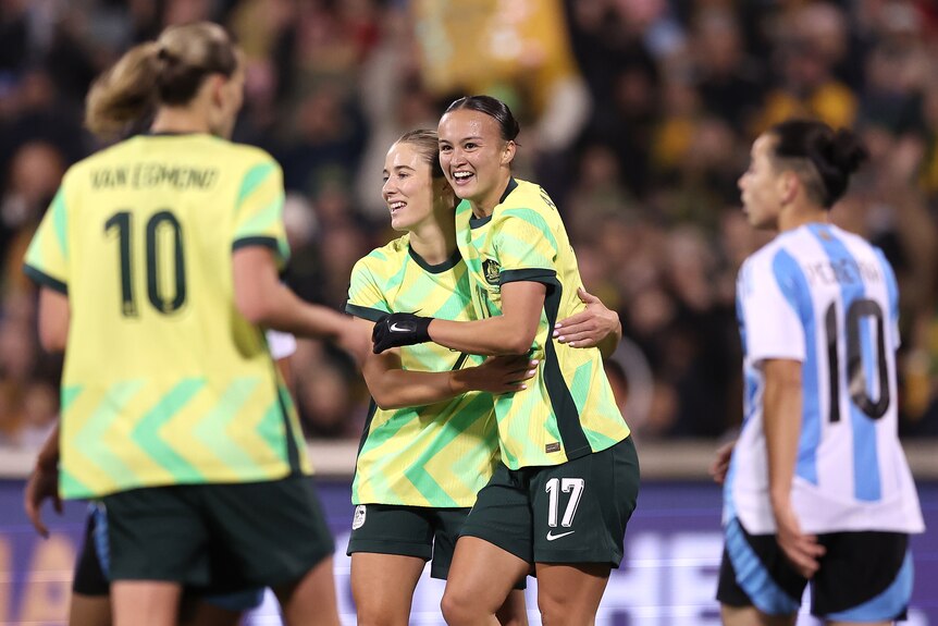 Two players in green and gold celebrate a goal.