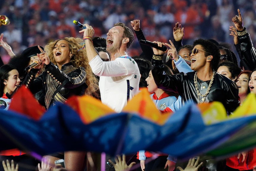 Beyoncé, Chris Martin and Bruno Mars sing on stage with a rainbow flag