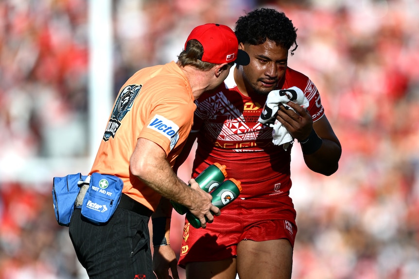 Eliesa Katoa of Tonga, holding a towel and bleeding with head injuries is attended to by a trainer.