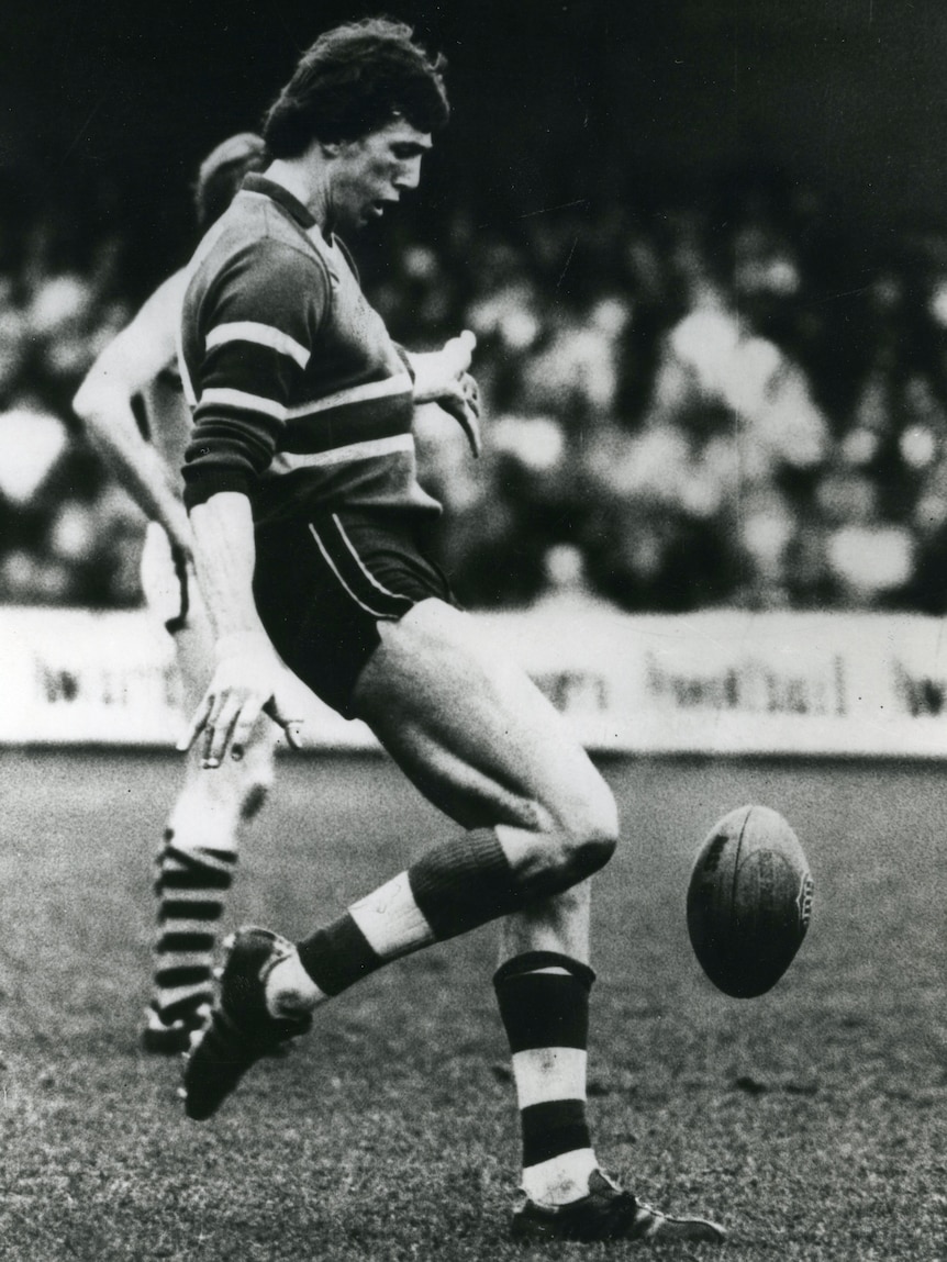 A black-and-white photo of a VFL footballer kicking the ball.