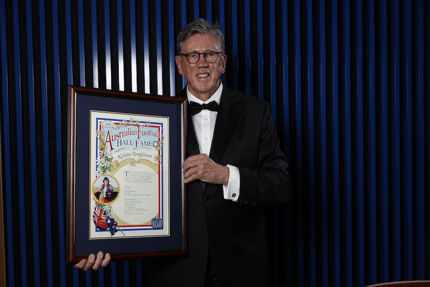 An older man in glasses holding a framed decorative certificate