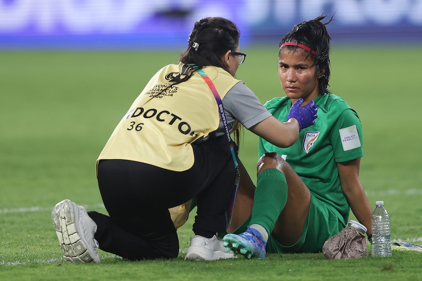 A goalkeeper in green receives treatment for a swollen cheekbone