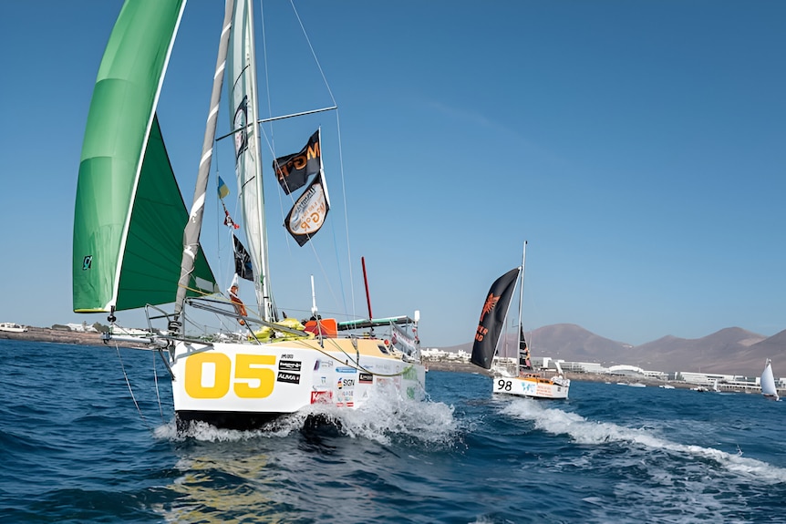 The Immortal Game sails ahead of another boat on the sea. A green sail is unfurled and filled with wind. 