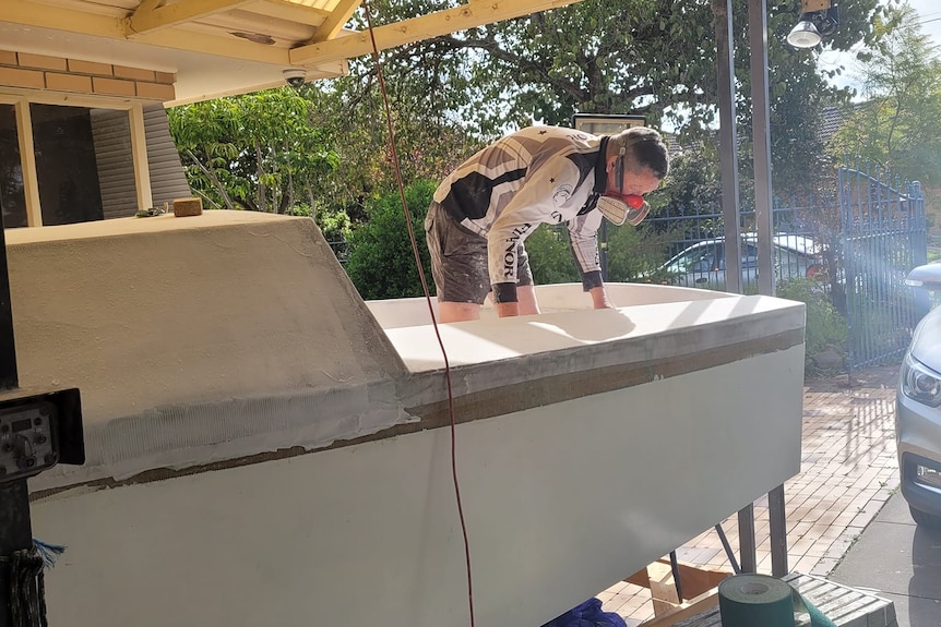 Dan Turner stands on the hull of the Immortal Game during its early construction at his Adelaide home.