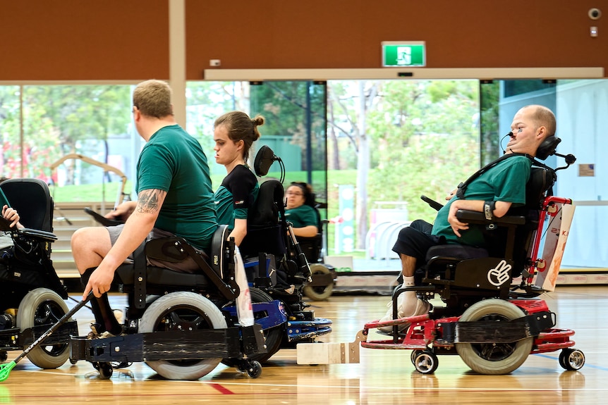Group of players in green in motorised wheelchair on court holding sticks