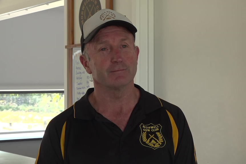 Man wearing a white cap, wearing a black and gold polo inside a clubroom.