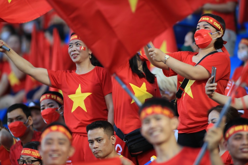 Vietnam fans cheer, they're wearing red shirts with yellow stars, and waving flags.