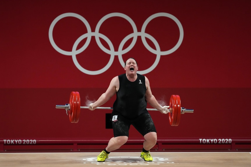 Weightlifter Laurel Hubbard drops the bar behind herself as she competes in front of the Olympic rings.