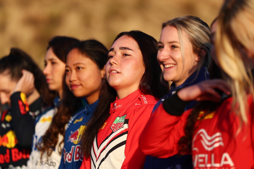 A row of young women in racing suits without helmets.