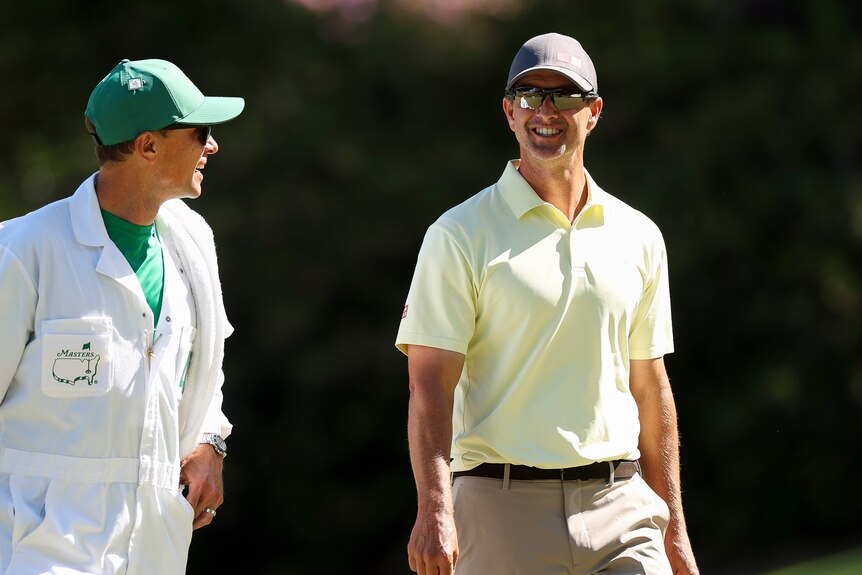 Adam Scott and his caddy smile as they walk the Masters course.