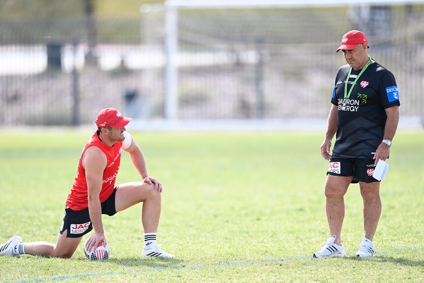 Dragons player Kyle Flanagan stretches as coach Shane Flanagan stands nearby at training.