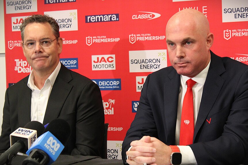 Two men sit at a table during a press conference.